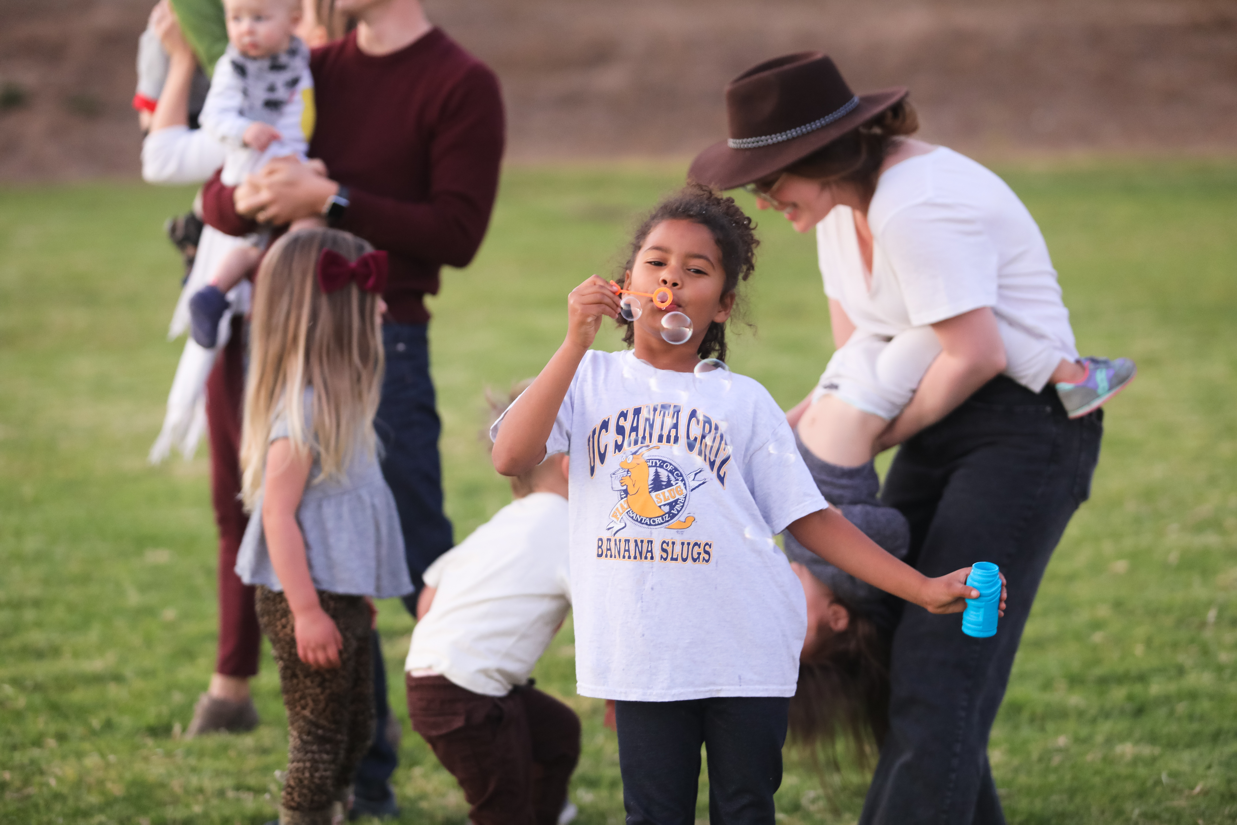 Photo of child blowing bubbles in Family Student Housing Field with other kids and adults