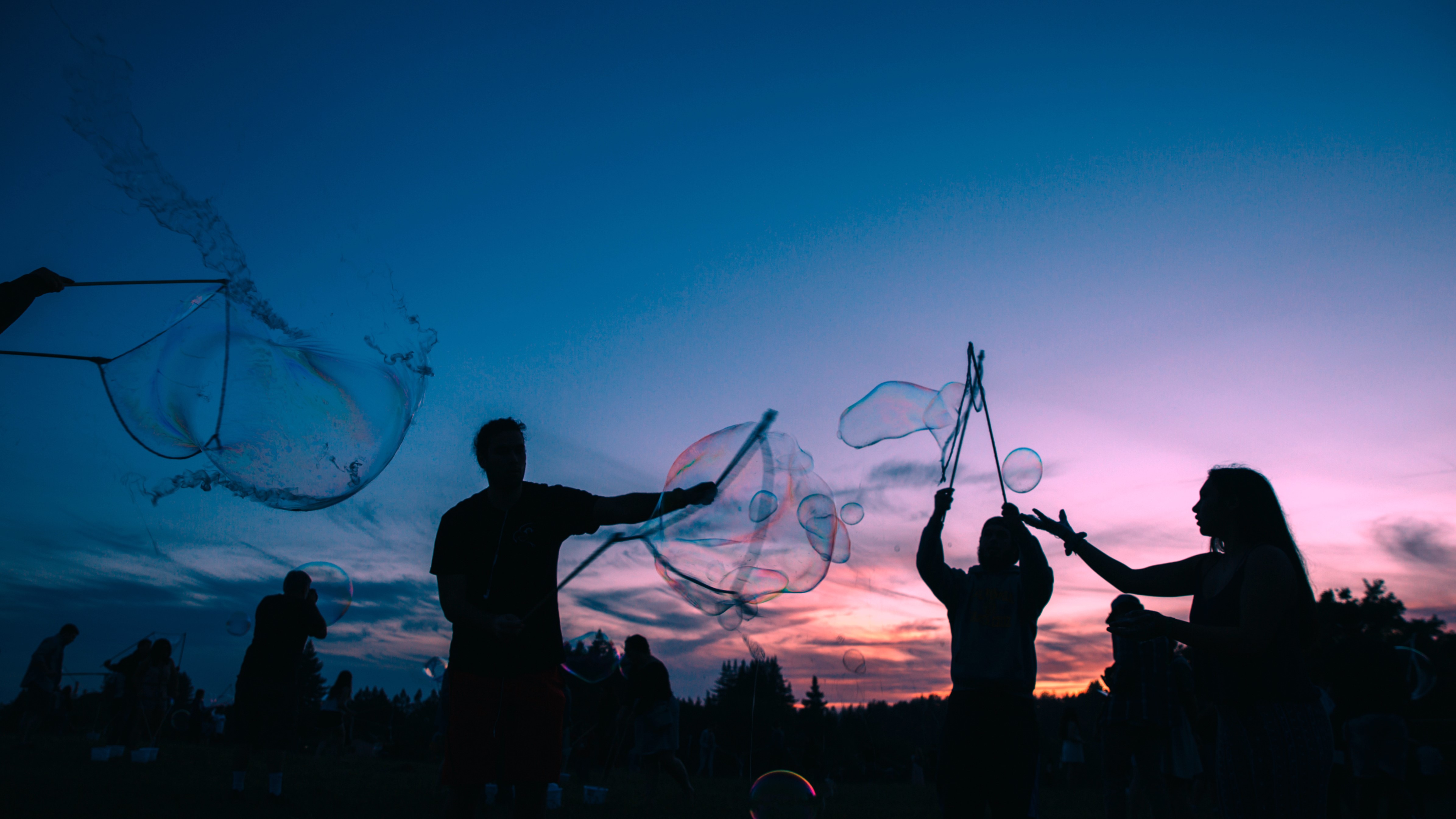 Sunset photo of silhouettes of students blowing large bubbles 