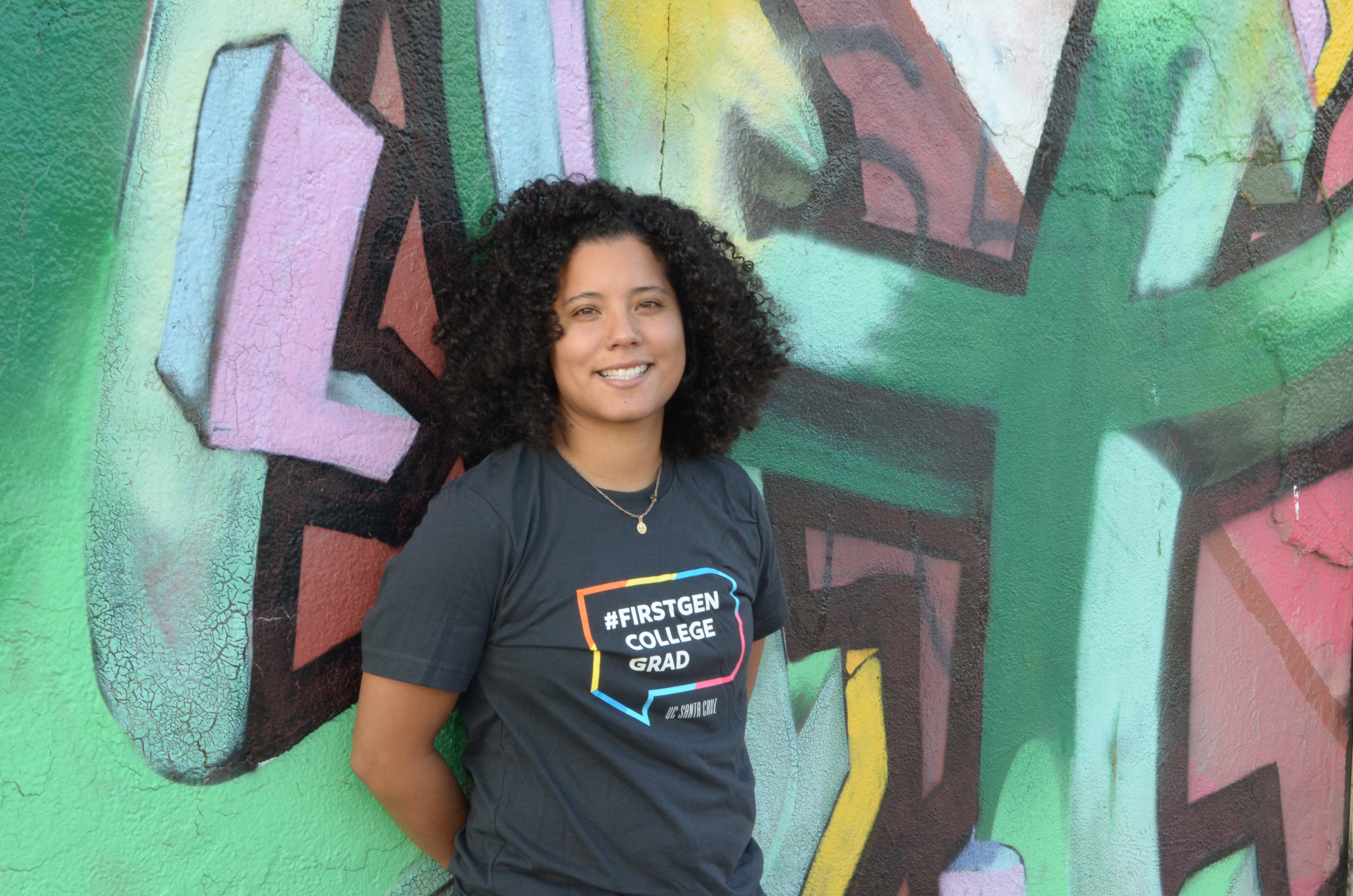 andrea vasquez smiling in front of artwork in first gen shirt