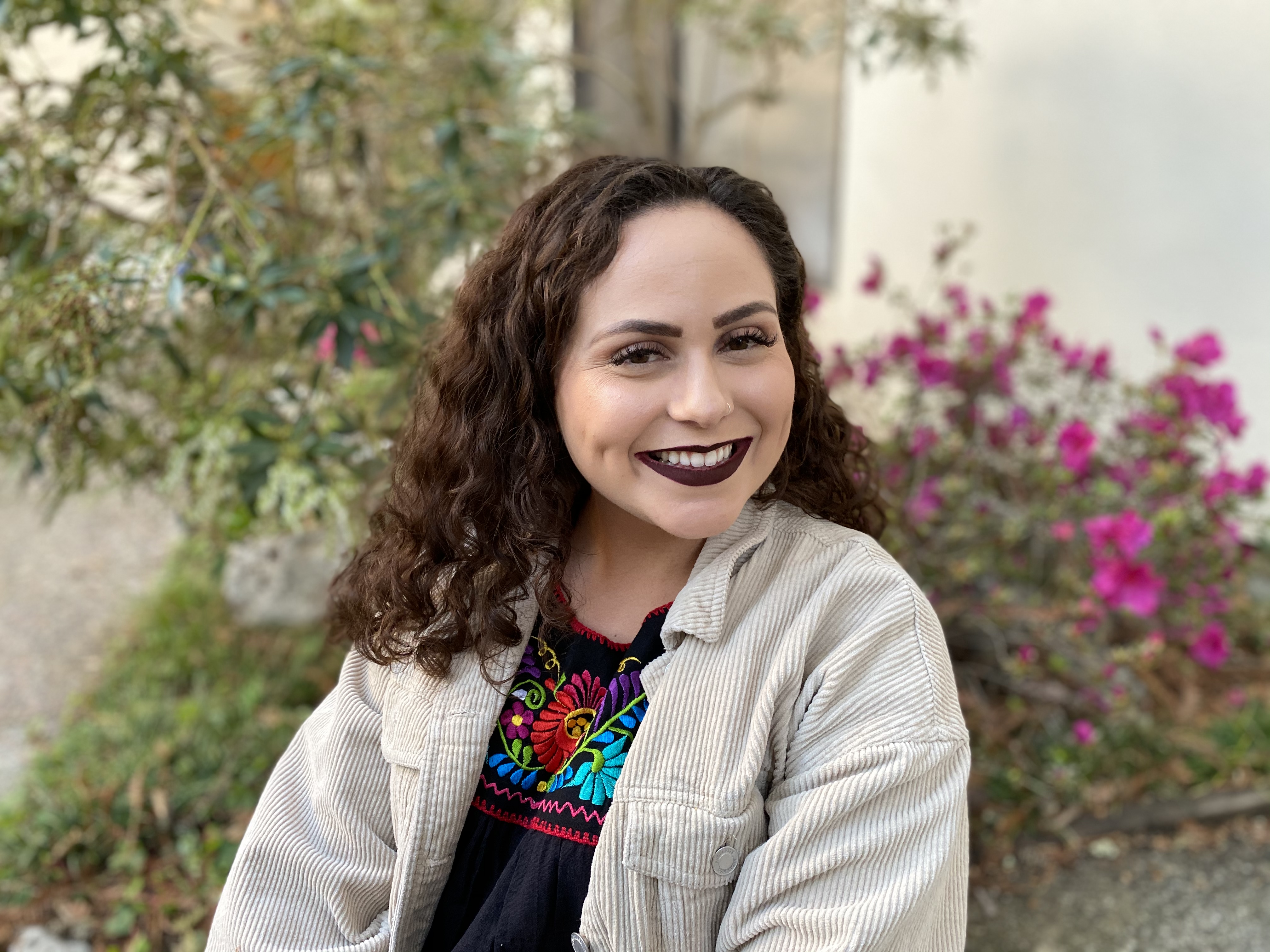 photo of bianca del toro smiling in corduroy, tan shirt in front of flowers