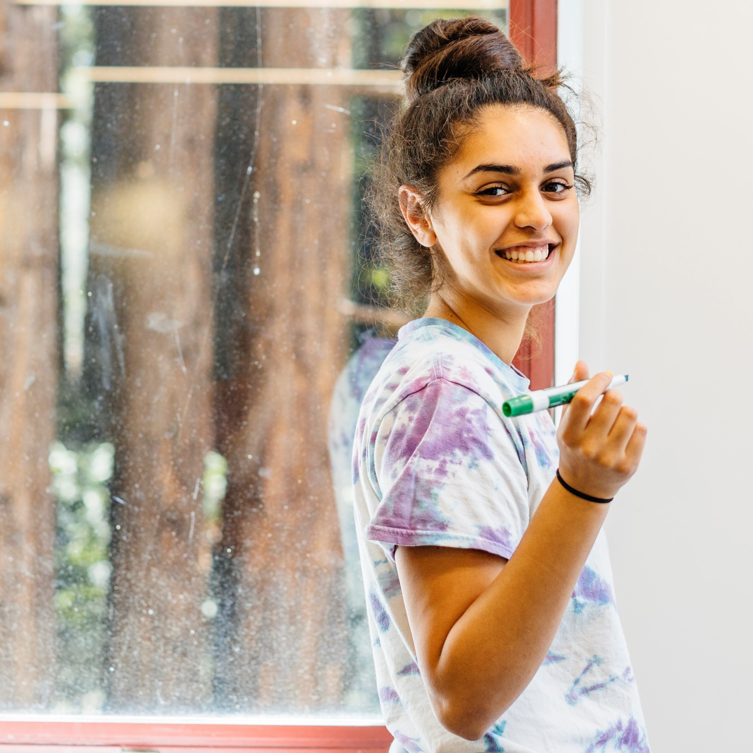 smiling student holding a dry-erase marker in front of a white board