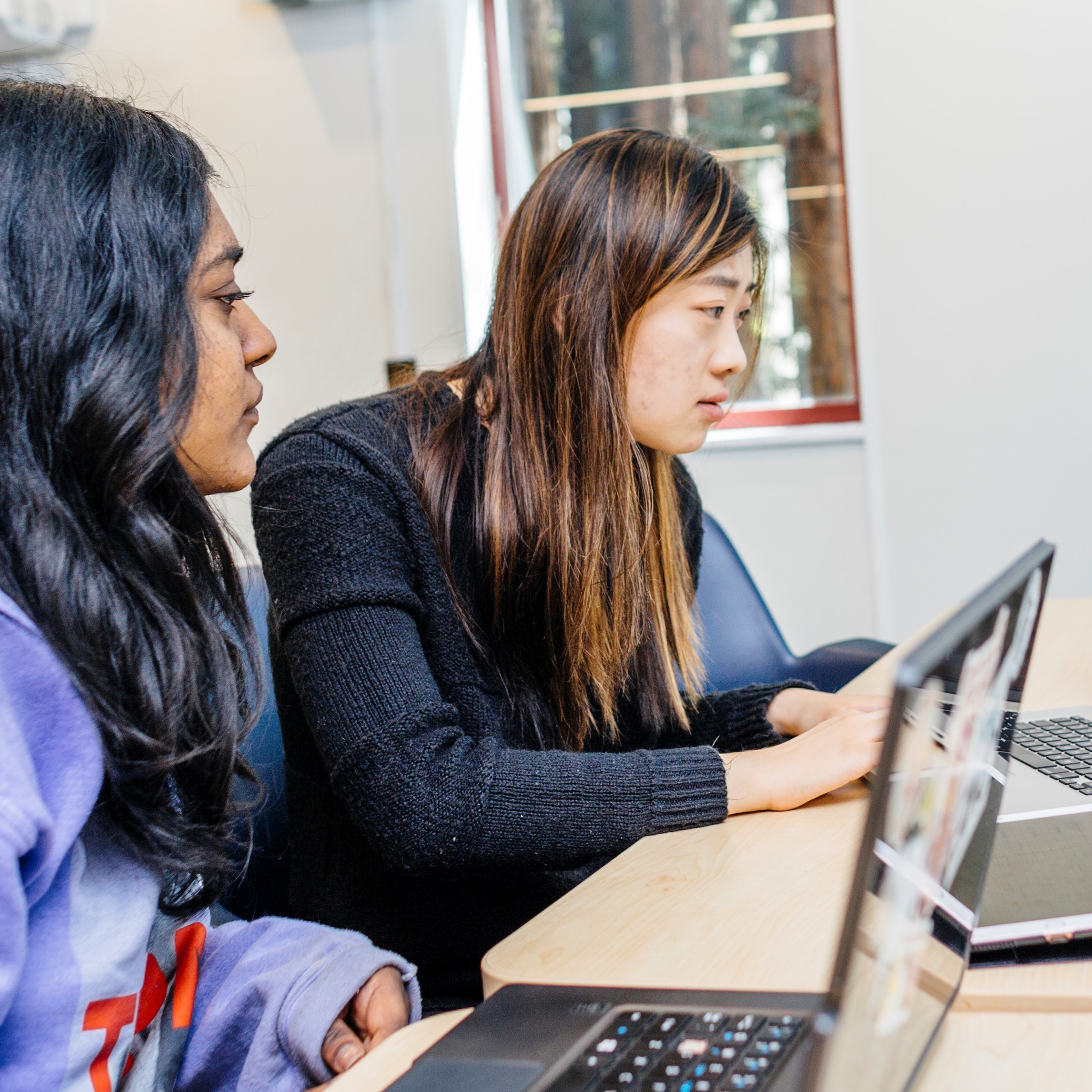 two students doing work at a desk on their laptops