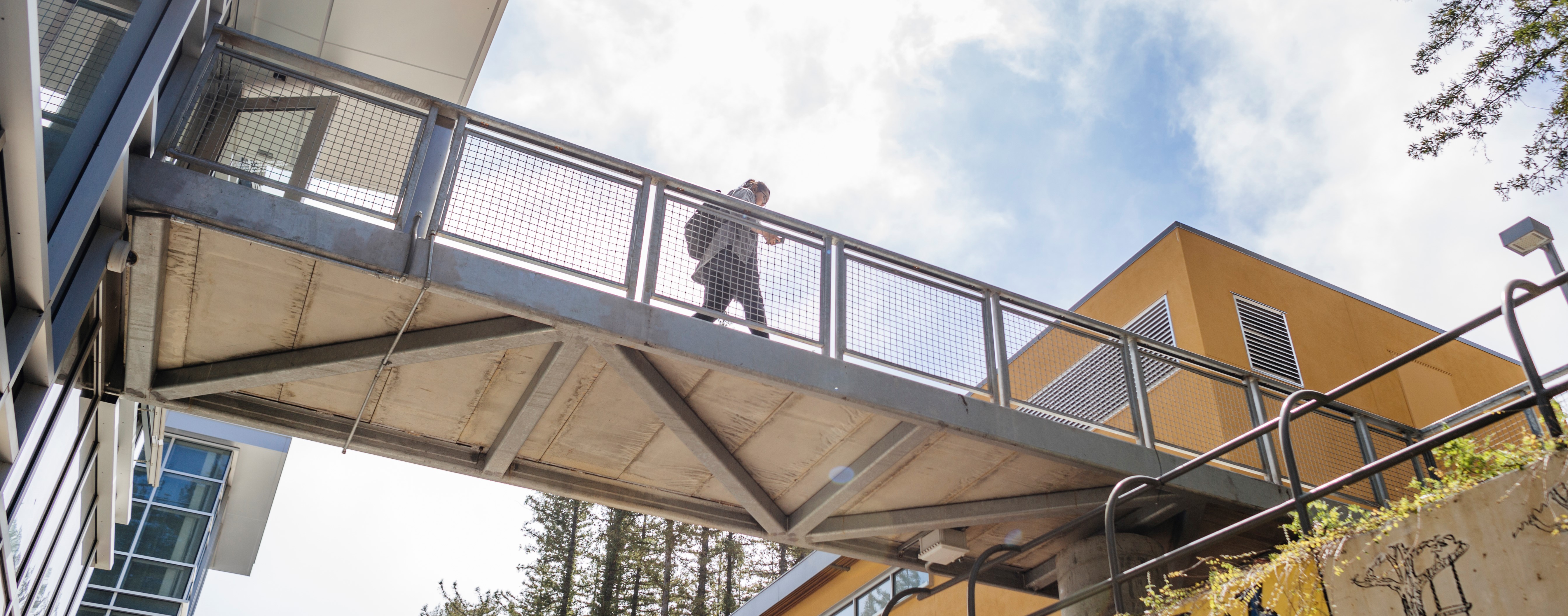 student crossing a metal bridge into an orange building